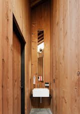 The bathroom set-up echoes that of the kitchen. A single-bowl, apron-front sink sits on a thin steel shelf, with exposed plumbing and separate hot and cold taps. The tall, slim inset mirror conceals a medicine chest in the bottom portion.