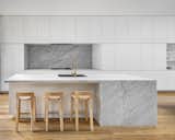 A large, marble island is the focal point of this all-white kitchen, with the marble backsplash helping to tie the space together.